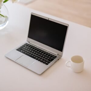 A minimalist workspace with an open laptop, coffee mug, and vase on a bright indoor table.
